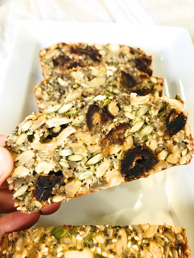 holding a slice of gluten free seed bread up close to show the density, seeds and nuts