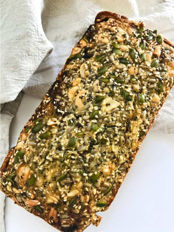 flat lay of a glolden brown cooked seed loaf full of nuts and seeds
