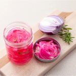 pickled red onions siting on a timber board