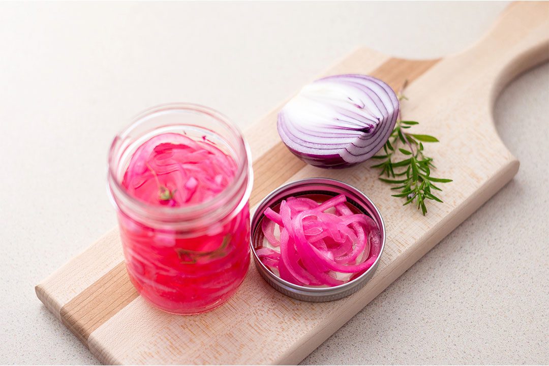 pickled red onions siting on a timber board