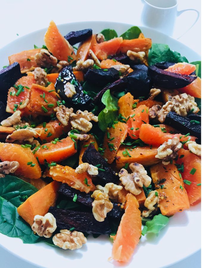 roasted beetroot and sweet potato salad with walnuts and oranged slices sitting in a large flat bowl