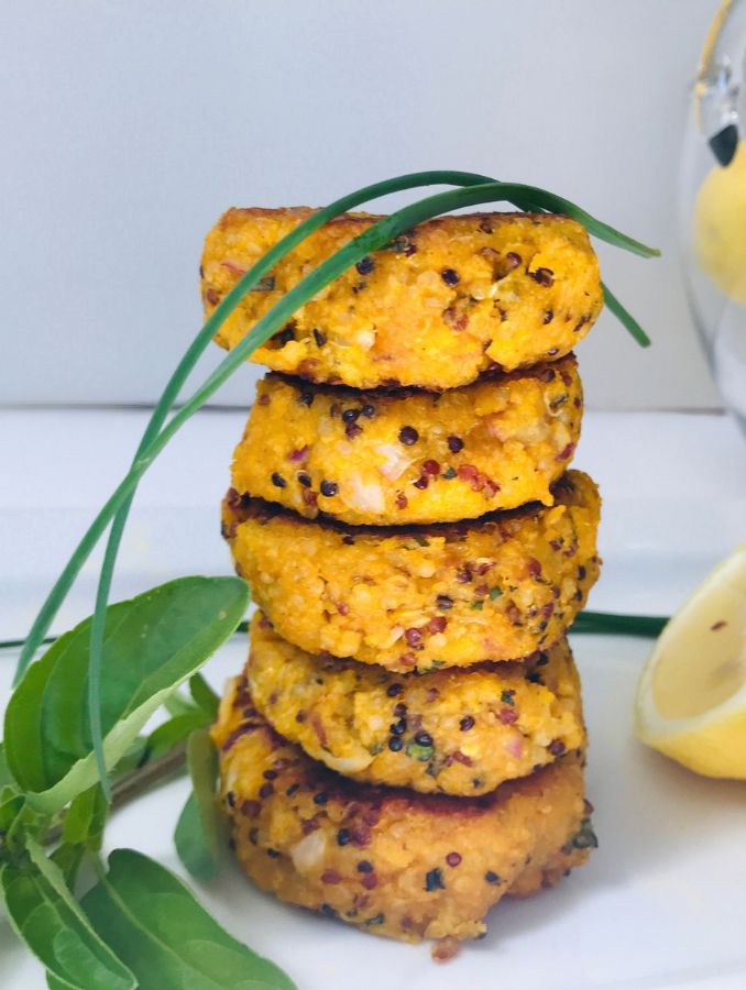 roasted pumpkin and quinoa patties on top of each other on a white plate with lemon wedges and a sprig of basil